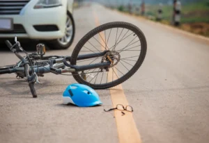 A fallen bicycle on the road with a stopped car behind it.